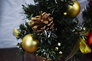 Close-up of mini Christmas tree with snow-dusted needles, gold pine cones and ornaments