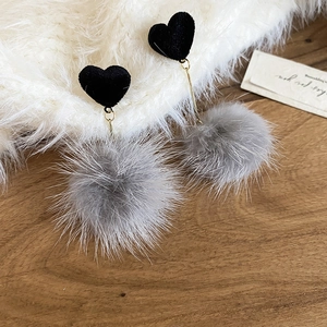 Dettaglio di orecchini a cuore neri con morbidi ciondoli a pompon grigi e metallo