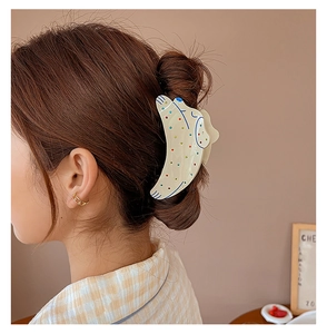 Side view of a woman wearing a cream acetate shark clip with colorful whale patterns