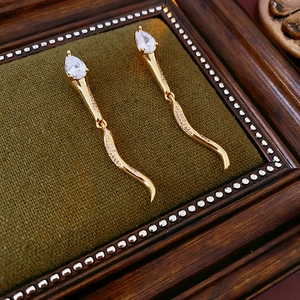 Close-up of gold-plated snake earrings with teardrop zirconia on dark velvet