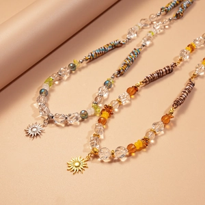 Détail de colliers bohèmes avec perles en verre et pendentifs soleil sur fond neutre