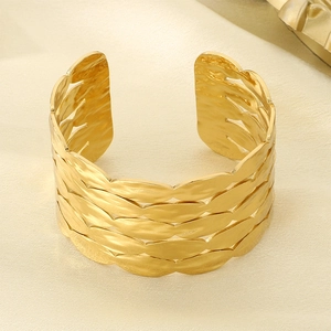 Detailed close-up of textured gold leaf patterns on a wide stainless steel cuff bracelet