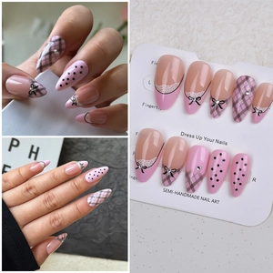 Detail of almond press-on nails with pink base, black bows, and rhinestones
