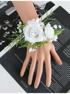 Detailed top view of a white artificial rose wrist corsage with green leaves on hand