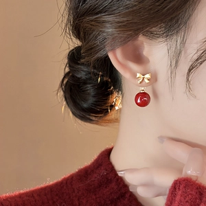 Detail of elegant gold bow and red bead earrings worn by a model in warm light
