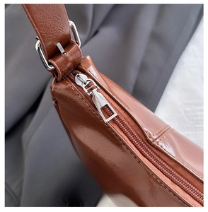 Close-up of smooth metal zipper and brown leather texture on a crescent shoulder bag