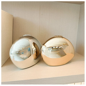 Polished silver and champagne gold metal egg-shaped crossbody clutch bags on wood
