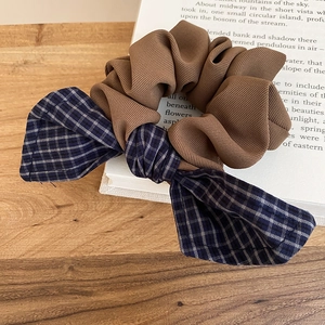 Detail of a brown ribbed fabric scrunchie with blue checkered bow on an open book