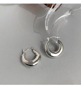 Vue détaillée des boucles d'oreilles créoles argentées polies sur surface en cuir foncé