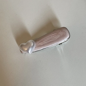 Détail de la pince à cheveux rose marbrée avec un ornement en forme de cœur nacré blanc