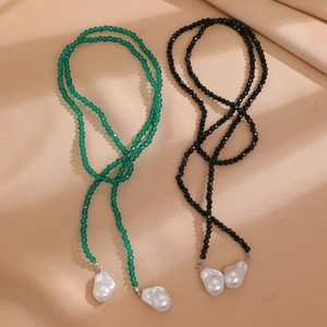 Detailed view of green and black beaded necklaces with baroque pearl pendants on silk fabric