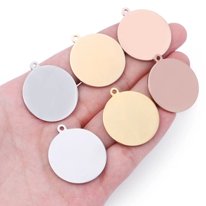 Close-up of hand holding round stainless steel pendants in silver, gold and rose gold colors