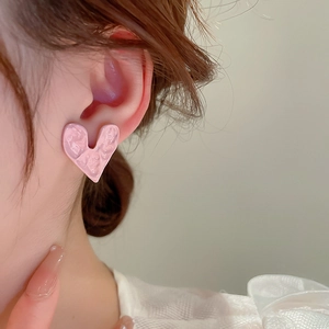 Close-up of heart-shaped pink earrings with pleated texture worn by a model