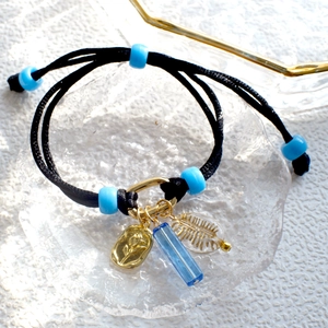Detail of black braided DIY bracelet featuring light blue beads and rose embossed pendants