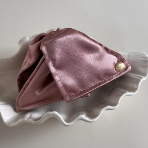 Détail d'une pince à cheveux en satin rose avec étiquette dorée sur plat coquille