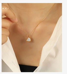Détail d'un collier pendentif cœur doré avec nacre blanche porté par un mannequin