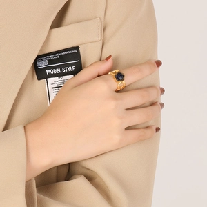 Detail of gold floral ring with deep blue gemstone worn on a model's hand with beige suit
