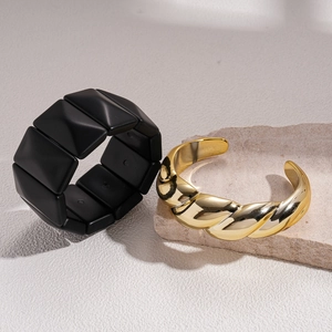 Minimalist twisted gold bangle and matte black stud bracelet set on natural stone