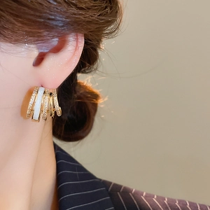 Close-up of gold-plated multi-layer C-shaped stud earrings with zircon and white enamel