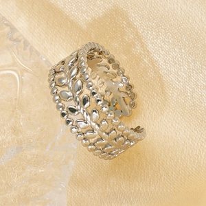 Macro shot of silver-toned hollow olive leaf ring on silk fabric with elegant lighting