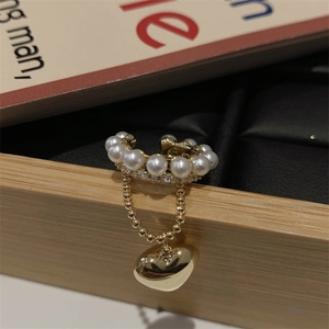 Dettaglio dell'ear cuff dorato con perle bianche, strass e ciondolo a cuore con nappine