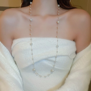 Macro detail of long gold-plated necklace featuring irregular white pearls on a fine chain