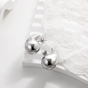 Macro shot of polished silver teardrop earrings on elegant lace background