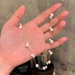 Detail of double-layer gold chain necklace with irregular pearls held by hand