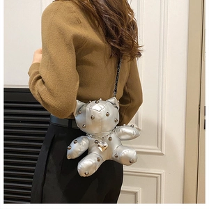 Detail of silver bear-shaped crossbody bag featuring metallic rivets and heart pendant