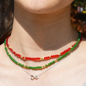 Close-up of layered red and green beaded necklaces with infinity symbol pendant charm