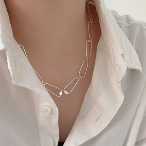 Detail of silver rectangular link chain necklace worn over a white minimalist shirt