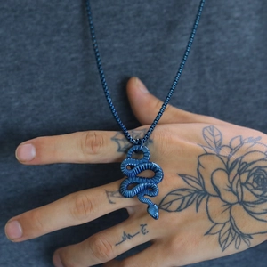 Close-up of a blue metallic snake pendant necklace worn on a person for detail