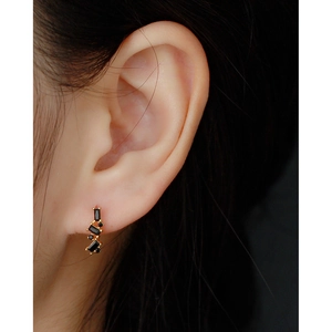 Close-up of golden geometric U-shape earrings with black zircon stones on ear