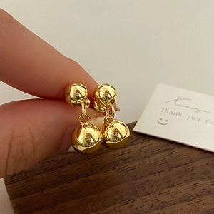 Detailed close-up of golden spherical earrings with a mirror-polished finish held by hand