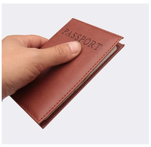 Detail of hand holding dark brown leather passport cover with debossed text and stitching