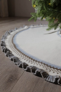 Close-up of beige knitted Christmas tree skirt with blue geometric patterns and ruffled edge