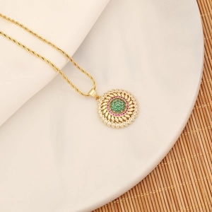 Detail of gold sunburst necklace with green center stone and pink gems on ceramic plate