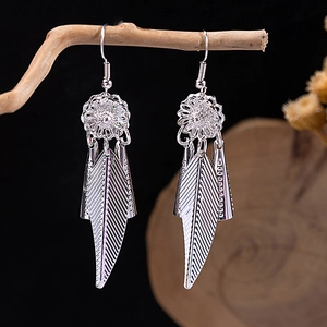 Detailed close-up of Bohemian silver flower earrings with feather tassel on wood branch