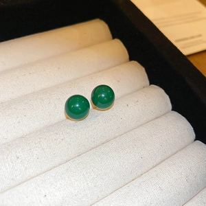 Close-up of green round bead stud earrings with golden base on white velvet display