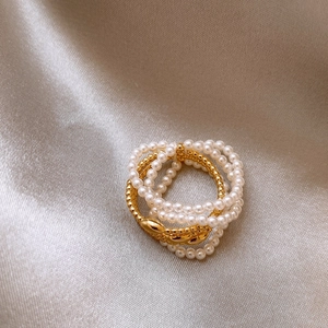 Close-up of gold-plated multi-layer pearl rings on elegant champagne silk fabric