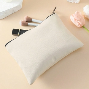 Top view of cream canvas makeup bag with black zipper near brushes and tulips