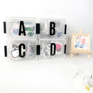 Detail view of 4 clear storage boxes with DIY letter stickers and a small wooden easel