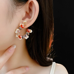 Close-up of vintage C-shaped gold earrings featuring colorful gemstones and small crystals