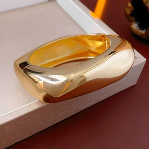 Close-up of golden irregular streamline wide bangle with mirror polished finish