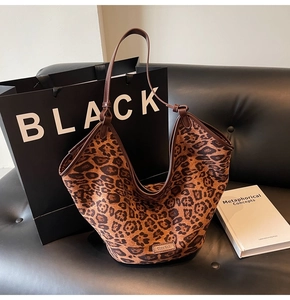 Detail of leopard print tote bag with brown handles on black leather sofa