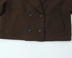 Detail view of dark brown double-breasted wool coat showing buttons and pocket texture