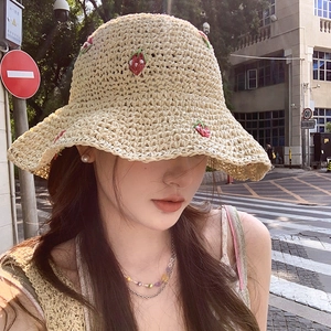 Beige straw bucket hat with red strawberry embroidery shown in a stylish urban street setting
