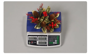 Détail d'un bougeoir de Noël de 43g avec pommes de pin et baies rouges sur une balance