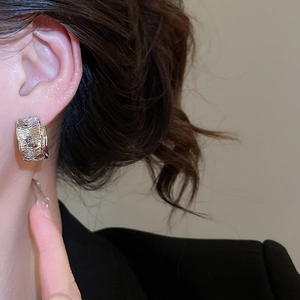 Close-up of silver C-shape textured earring with irregular lava pattern on model