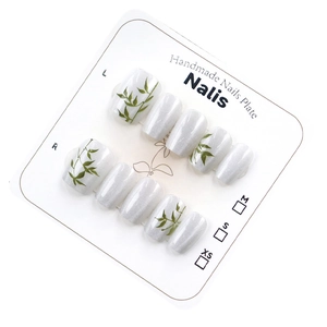 Handmade press-on nails with silver pearl base and green bamboo leaf art on display card